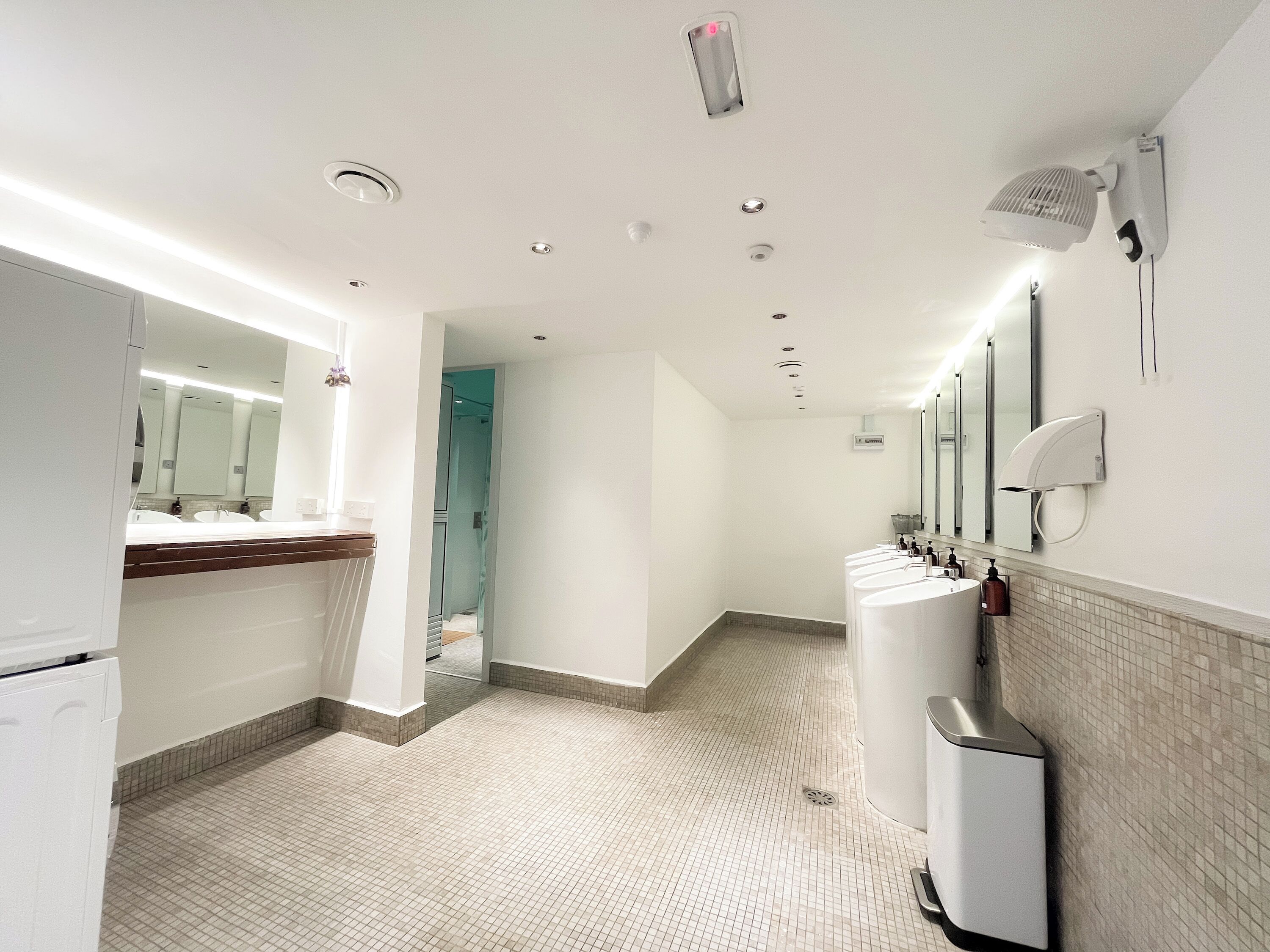 A modern bathroom with multiple sinks, a mirror, a hand dryer, and a ventilation system.