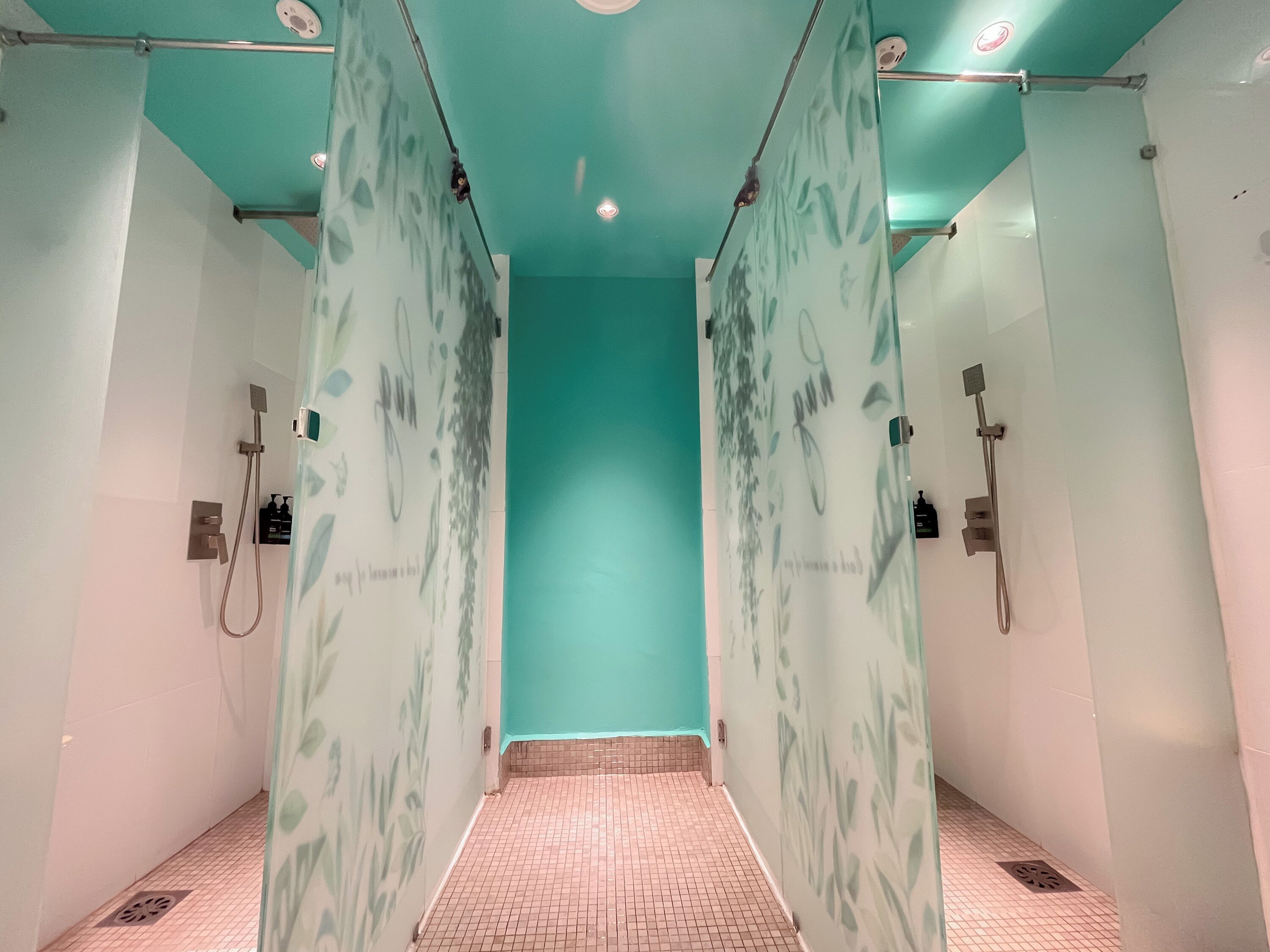 Une salle de bain moderne avec un mur turquoise, des portes de douche en verre et un sol carrelé.