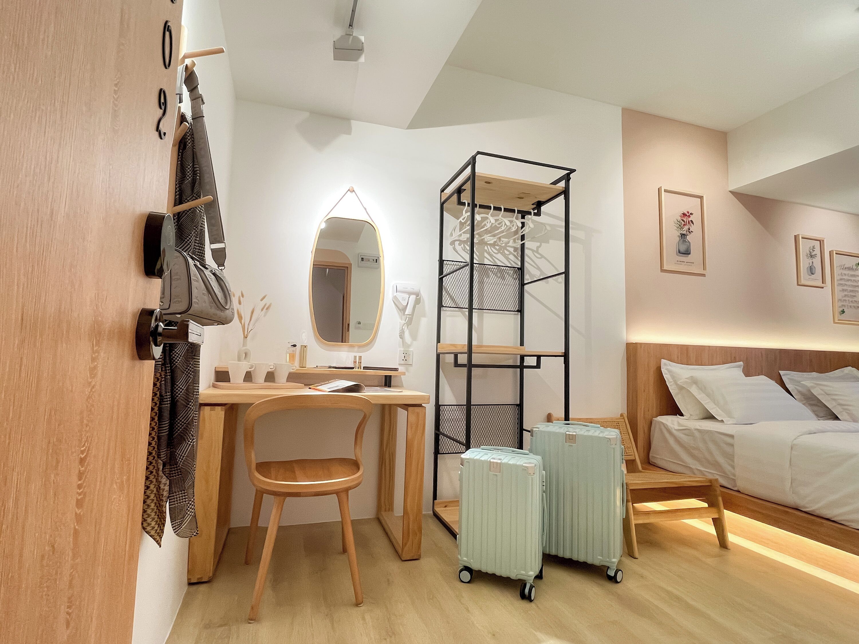 A modern hotel room with a wooden desk, a chair, a bed, and two wheeled luggage items.