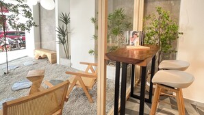 A modern interior with a wooden table, two bar stools, and a bench. There are potted plants and a magazine on the table. - Sleep Box Penang (George Town)