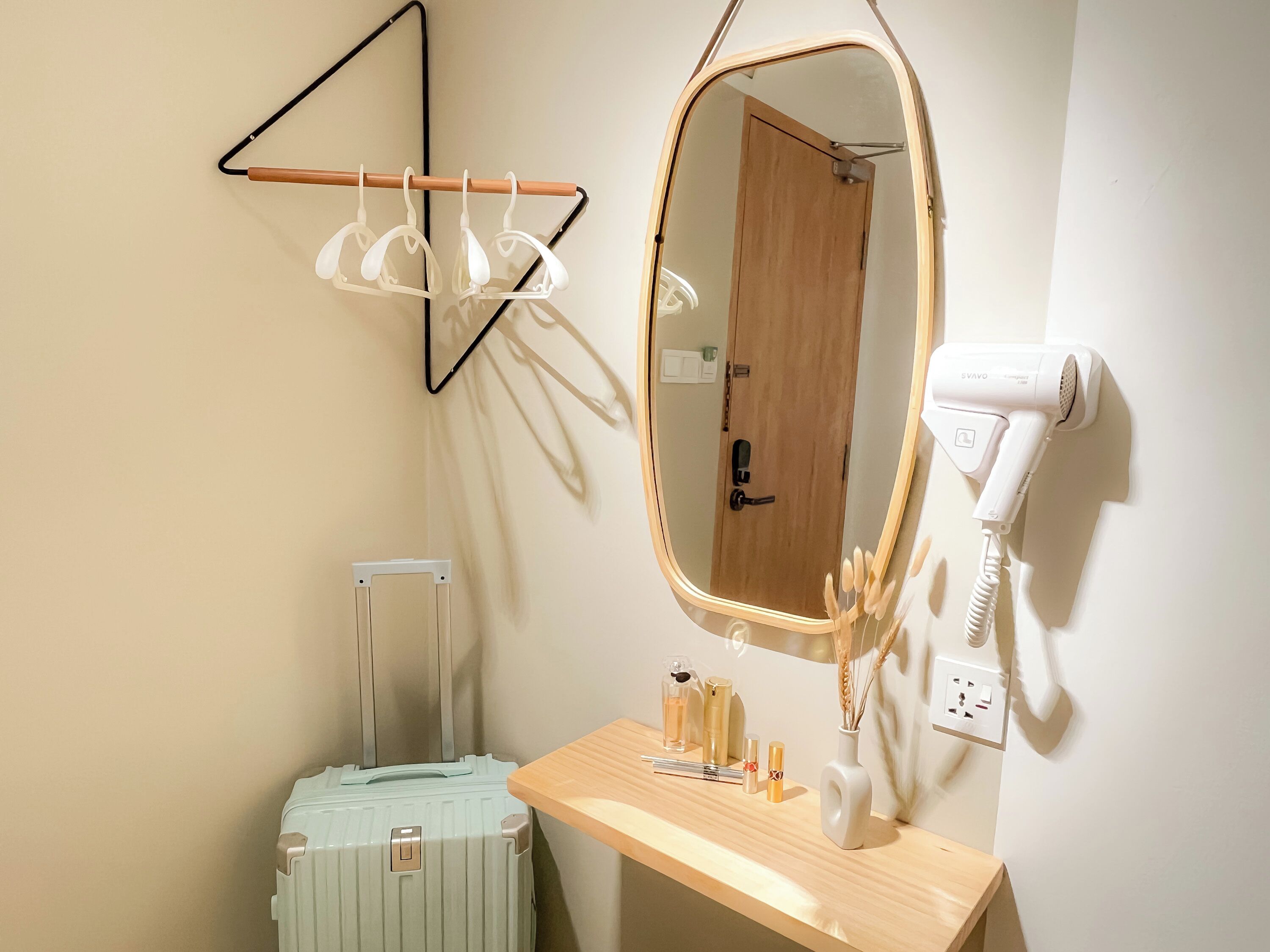A bathroom with a wooden vanity, a mirror, a hairdryer, a towel rack, and a suitcase.