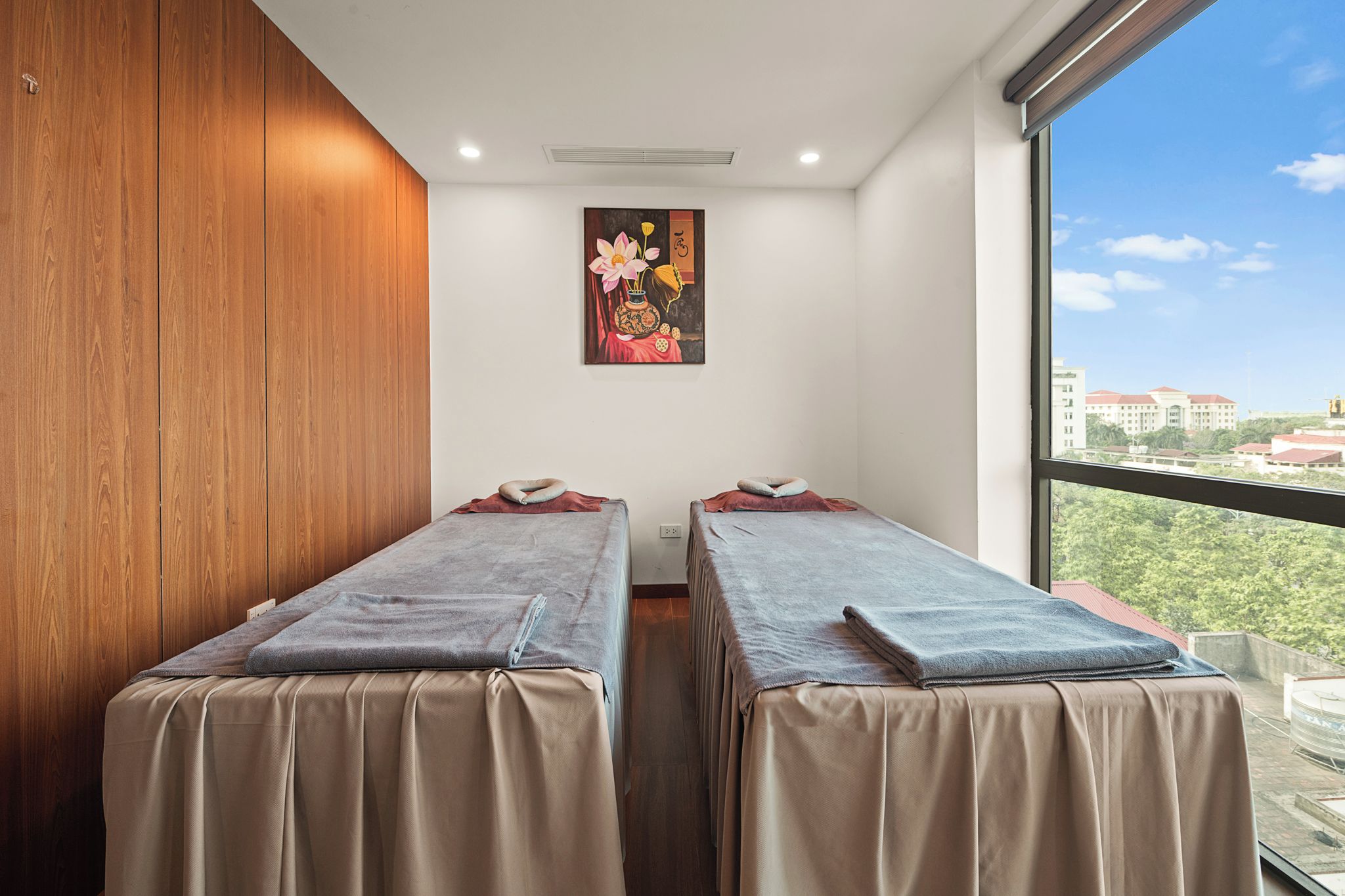Una habitación con dos camas, una pared de madera, un cuadro y vistas a edificios.