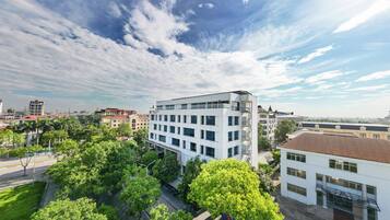 Un edificio moderno con techo plano, rodeado de exuberante vegetación y un cielo despejado con nubes dispersas.