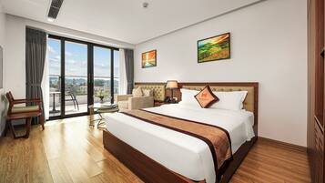 A hotel room with a large bed, a desk, a chair, and a view of the city through the windows.