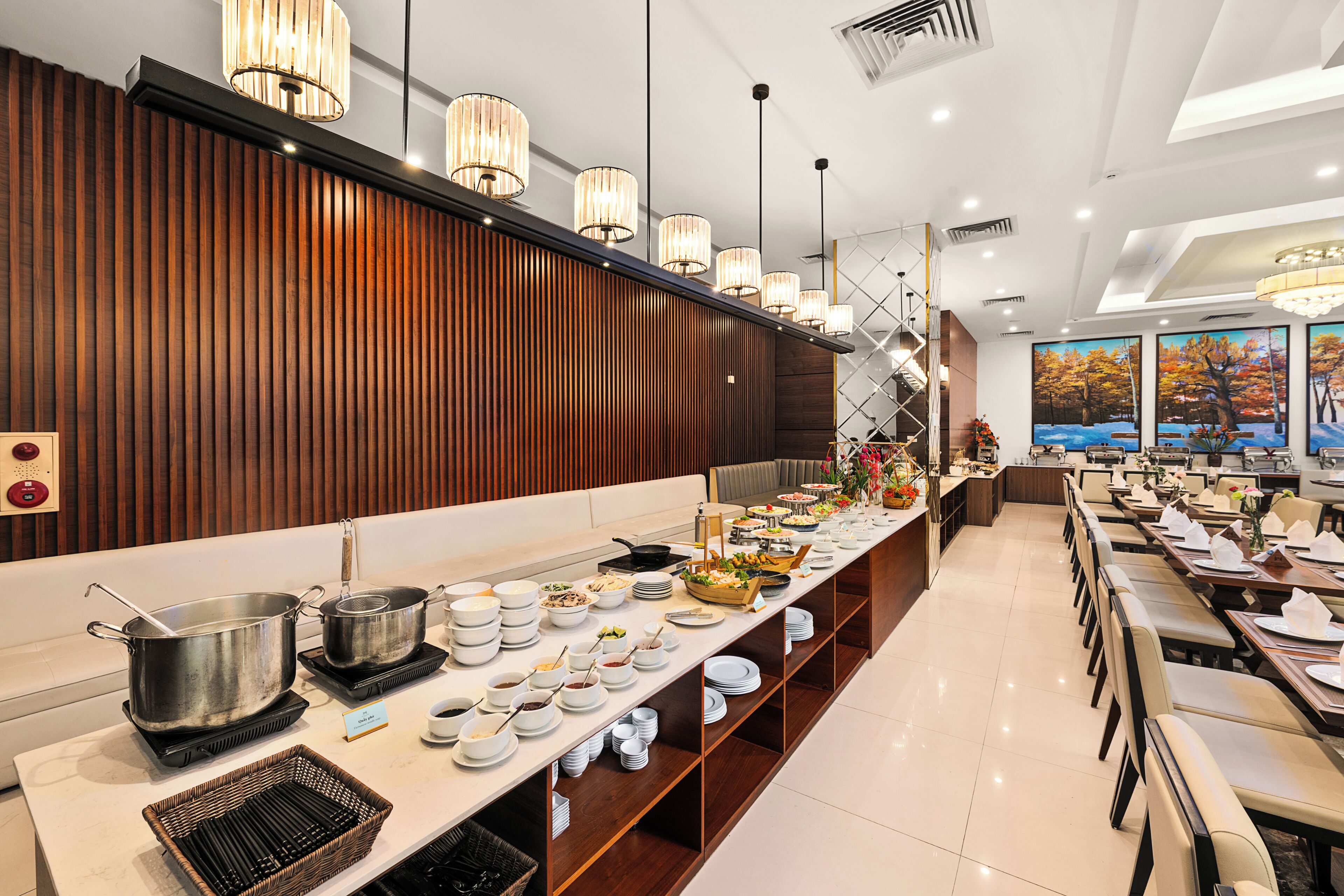 A buffet setup with multiple serving stations, a wooden panel wall, and a dining area with tables and chairs.