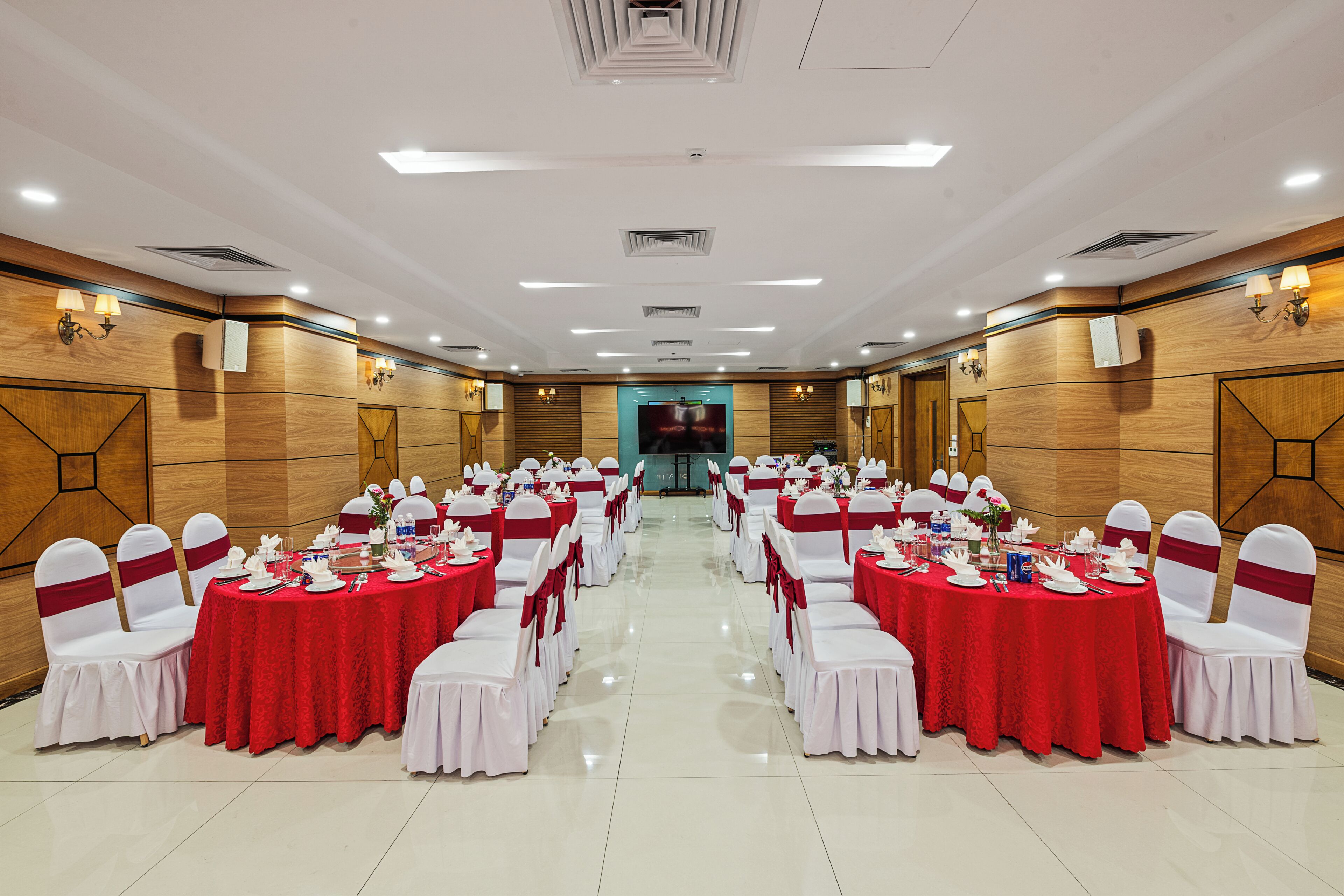 A banquet hall with round tables, white chairs, and red tablecloths.