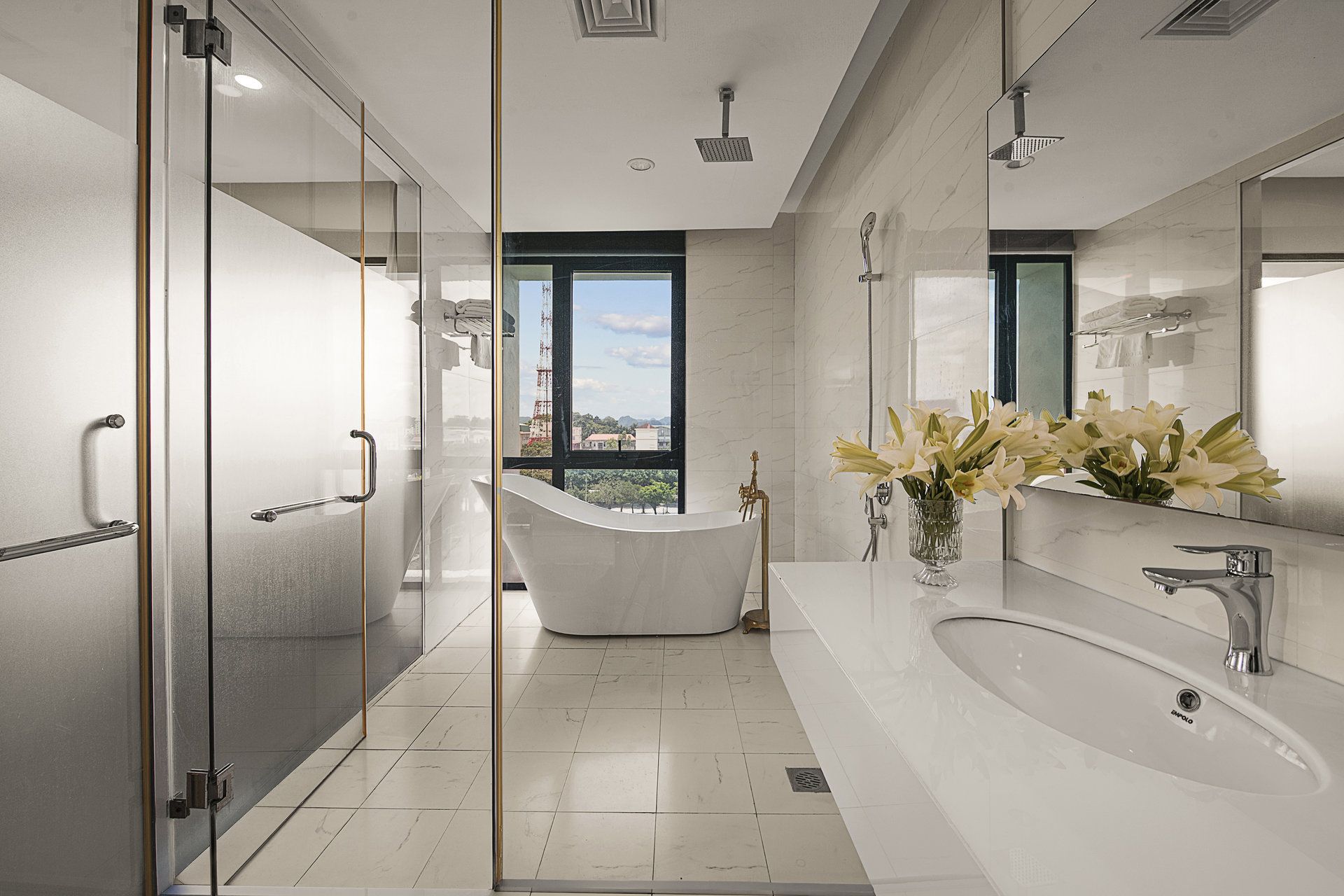A modern bathroom with a freestanding bathtub, a large mirror, and a window offering a city view.