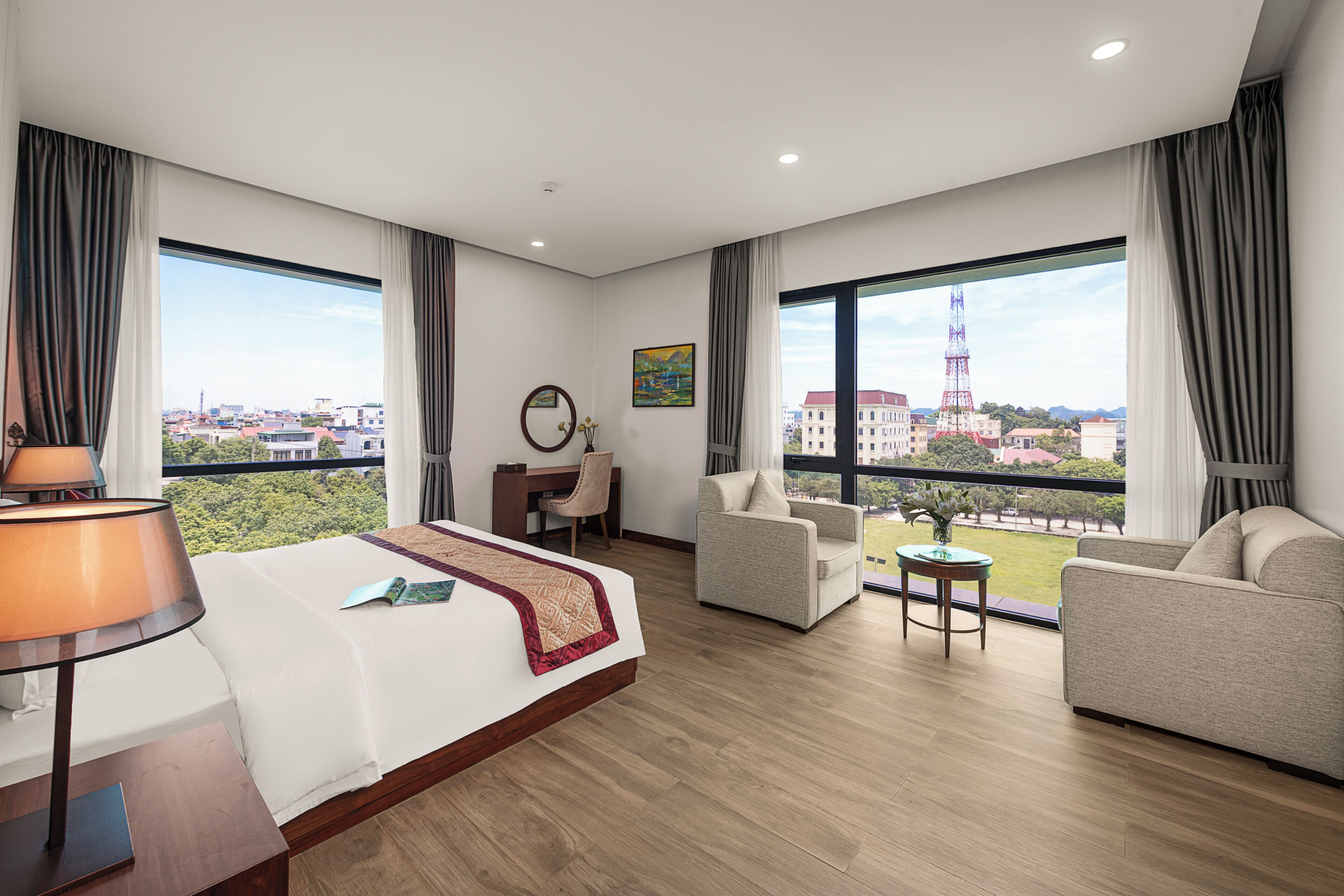 A hotel room with a large bed, two armchairs, a desk, and a view of a cityscape.