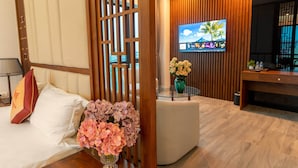 A hotel room with a bed, a TV mounted on the wall, a wooden partition, and a small table with a vase of flowers. - MT Collection Hotel (Hoa Lu)