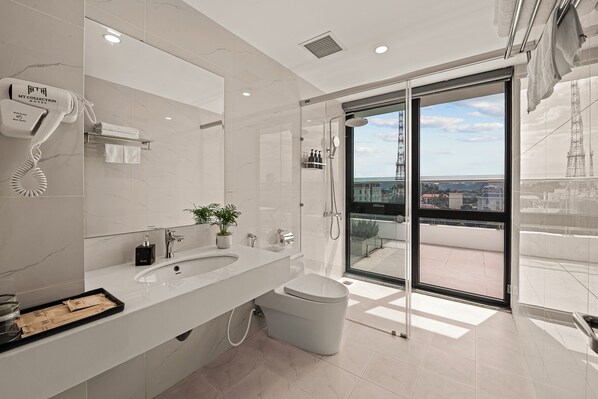 A modern bathroom with a large mirror, a hairdryer, a sink, a toilet, and a glass door leading to a balcony with a view. - MT Collection Hotel (Ninh Binh)
