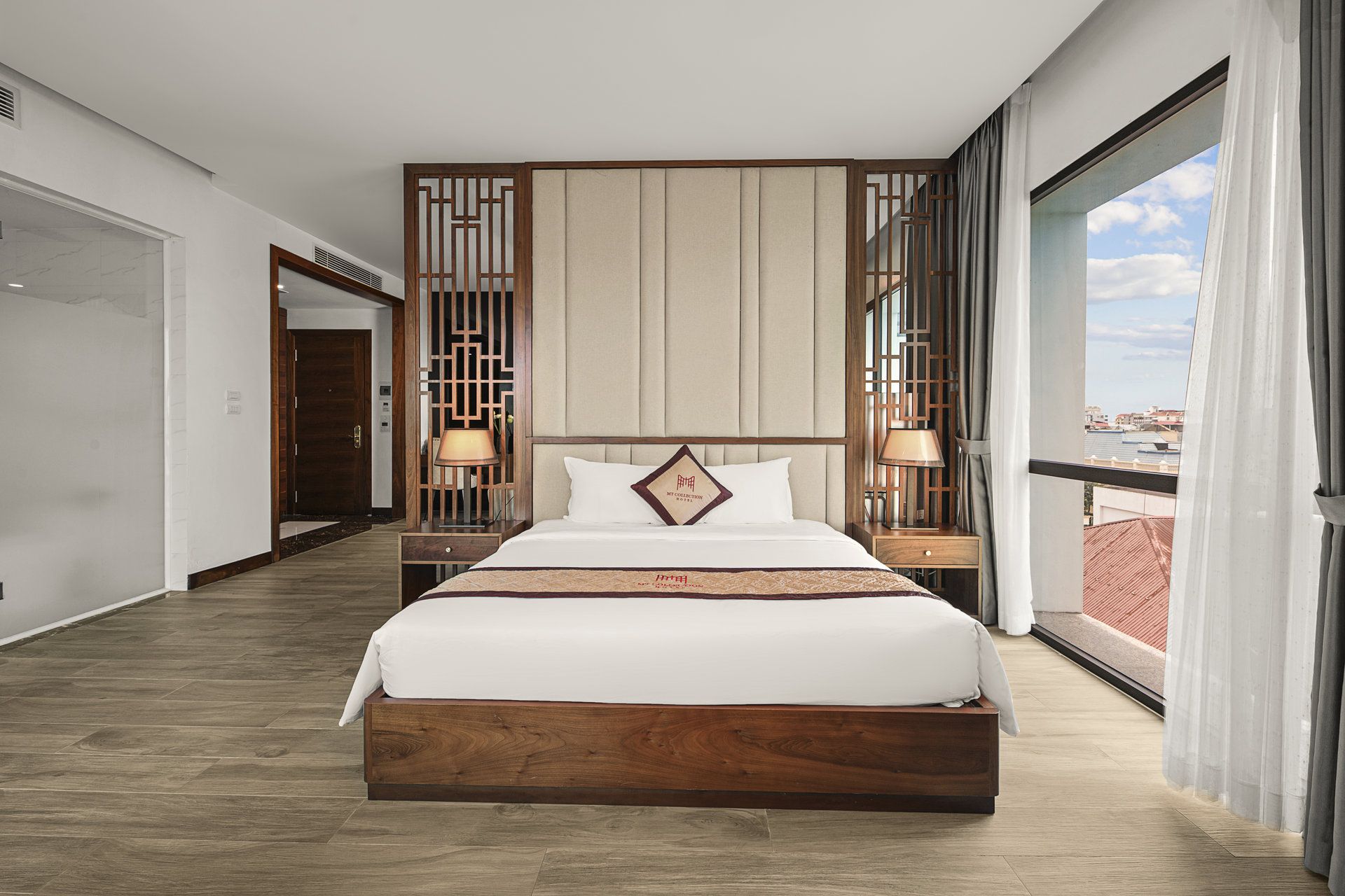 A hotel room with a large bed, wooden headboard, and a view through a window.