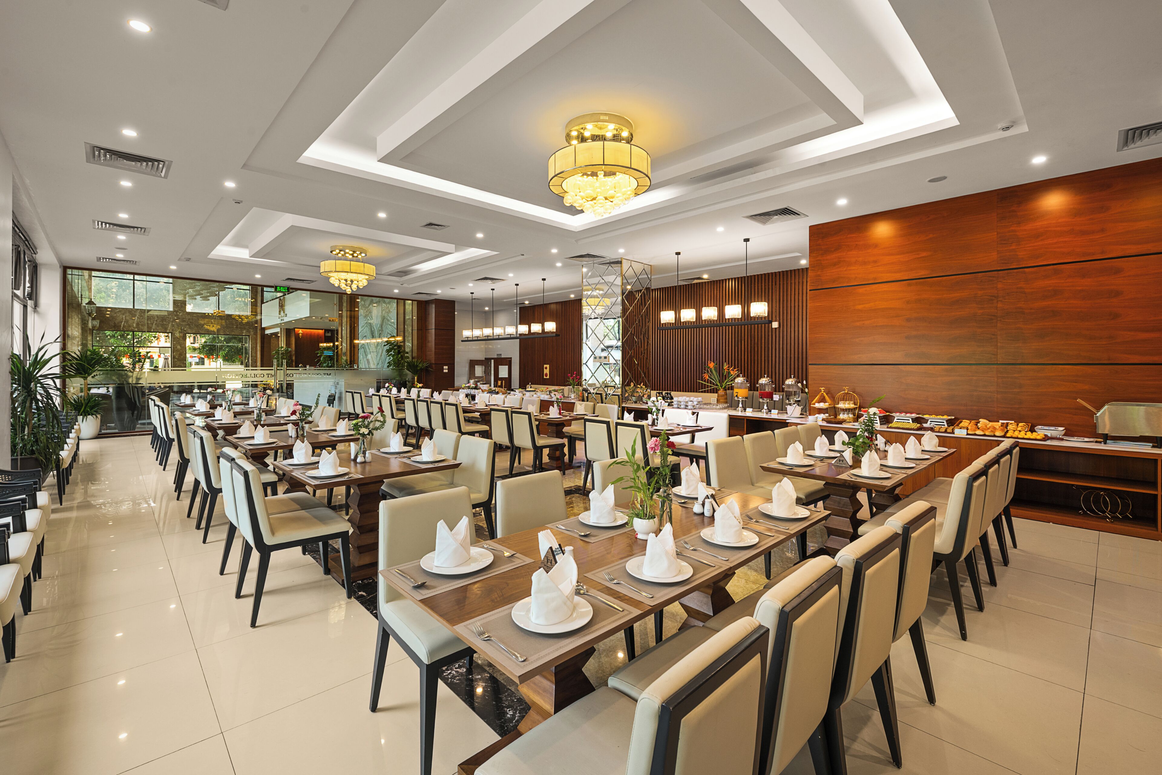 Un comedor amplio con mesas largas dispuestas para varios comensales, candelabros modernos y vistas al exterior a través de grandes ventanales.