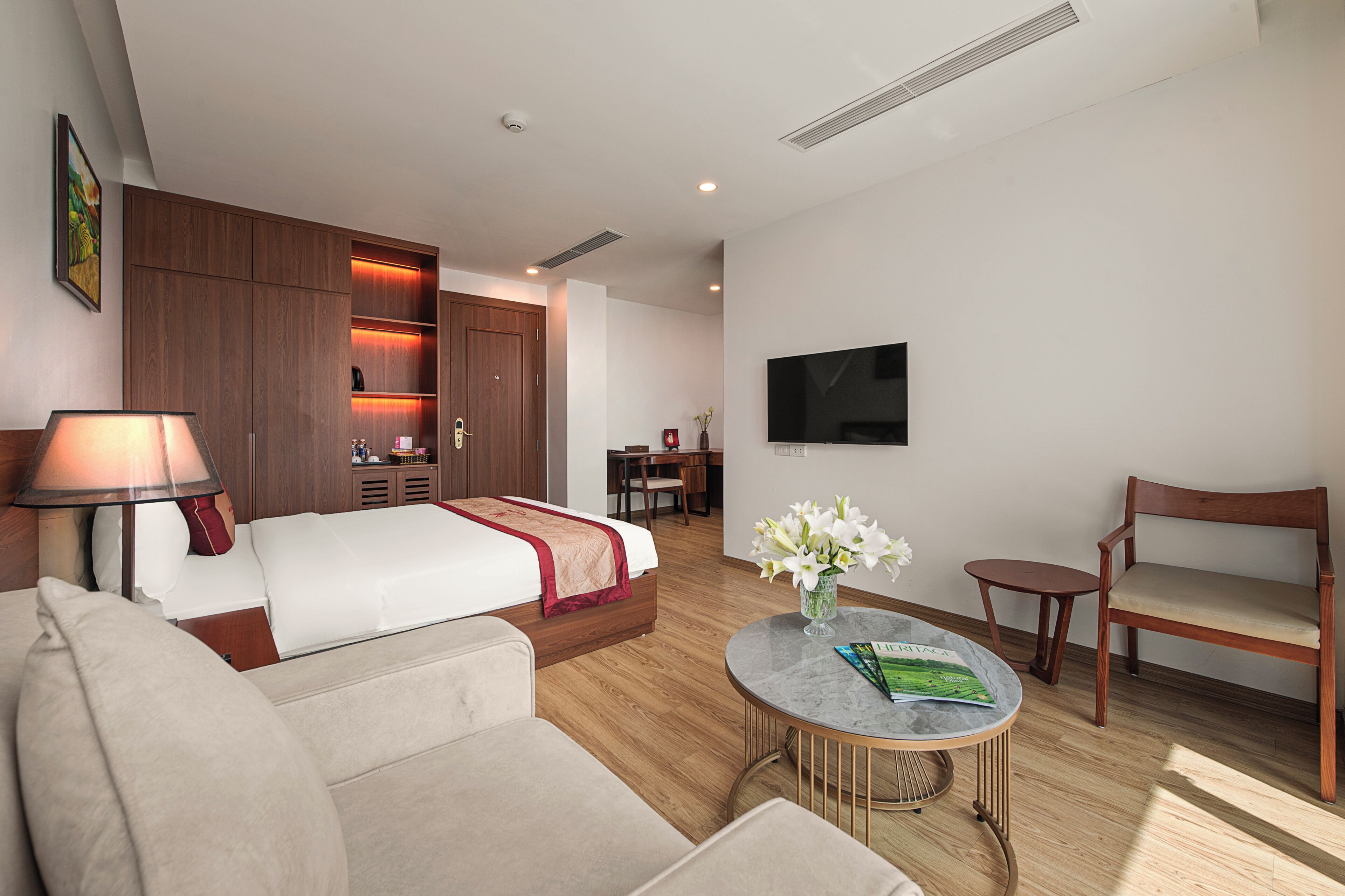 A hotel room with a bed, a sofa, a round coffee table, a TV, and a desk with a chair.