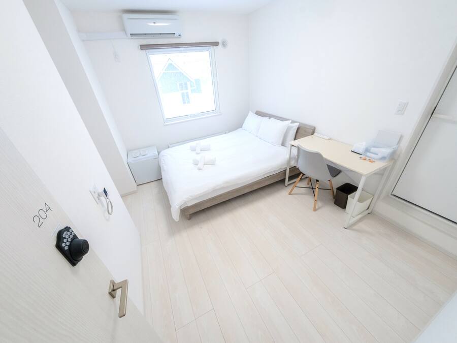 Un dormitorio moderno y minimalista con cama, escritorio y ventana con vista a una casa.