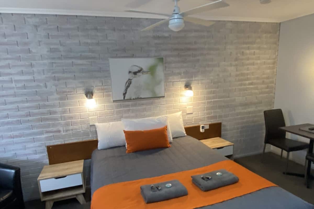 A modern hotel room with a brick-patterned wall, a bed with an orange blanket, two bedside tables, a desk, and a chair.