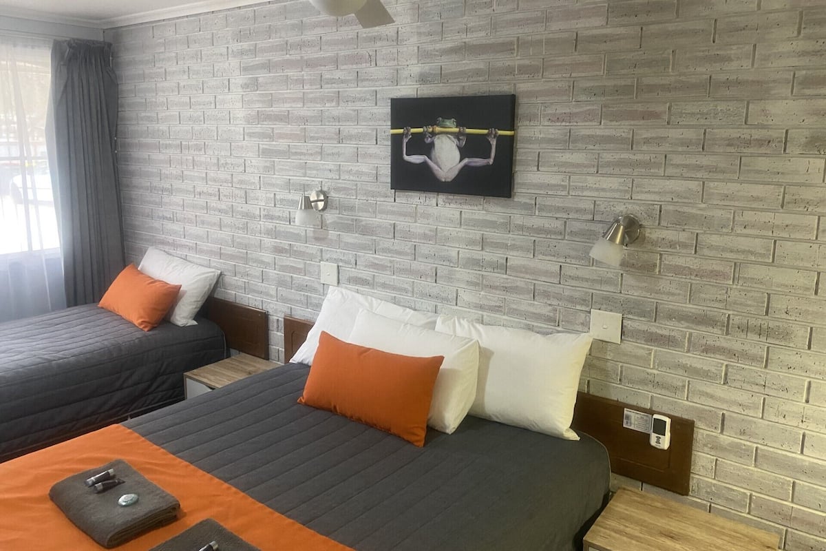 A hotel room with two beds, a brick wall, a ceiling fan, and a painting.