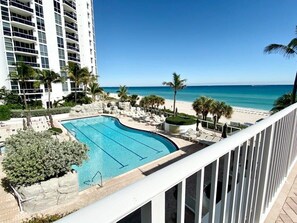 A swimming pool with lounge chairs and palm trees, overlooking a beach and ocean. - Elegant Resort Studio with Breathtaking Views (Sunny Isles Beach)