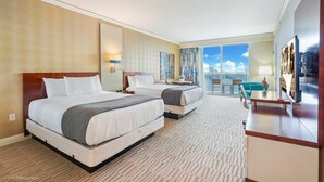 A hotel room with two beds, a desk, a chair, a TV, and a balcony with a view.