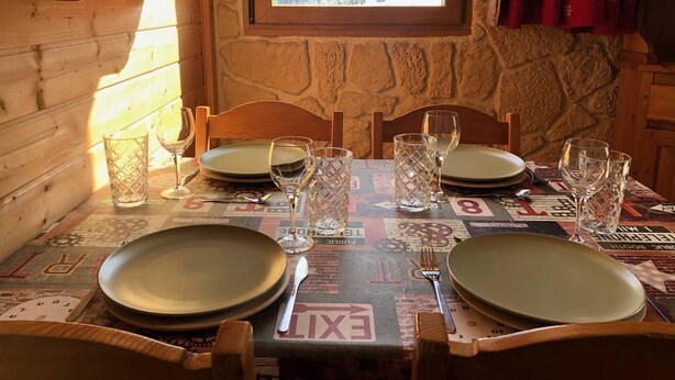 A wooden interior with a table set for two, a window with a snowy view, and stone walls. - La Clairière 1 - Cosy studio with a beautiful view of the resort (LES AVANCHERS VALMOREL)