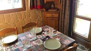 A dining table set with plates, glasses, and cutlery, a wooden cabinet with glass doors, and a stone wall. - La Clairière 1 - Cosy studio with a beautiful view of the resort (LES AVANCHERS VALMOREL)