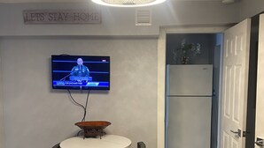Un comedor con una mesa redonda, dos sillas, un televisor montado en la pared y una lámpara en el techo.