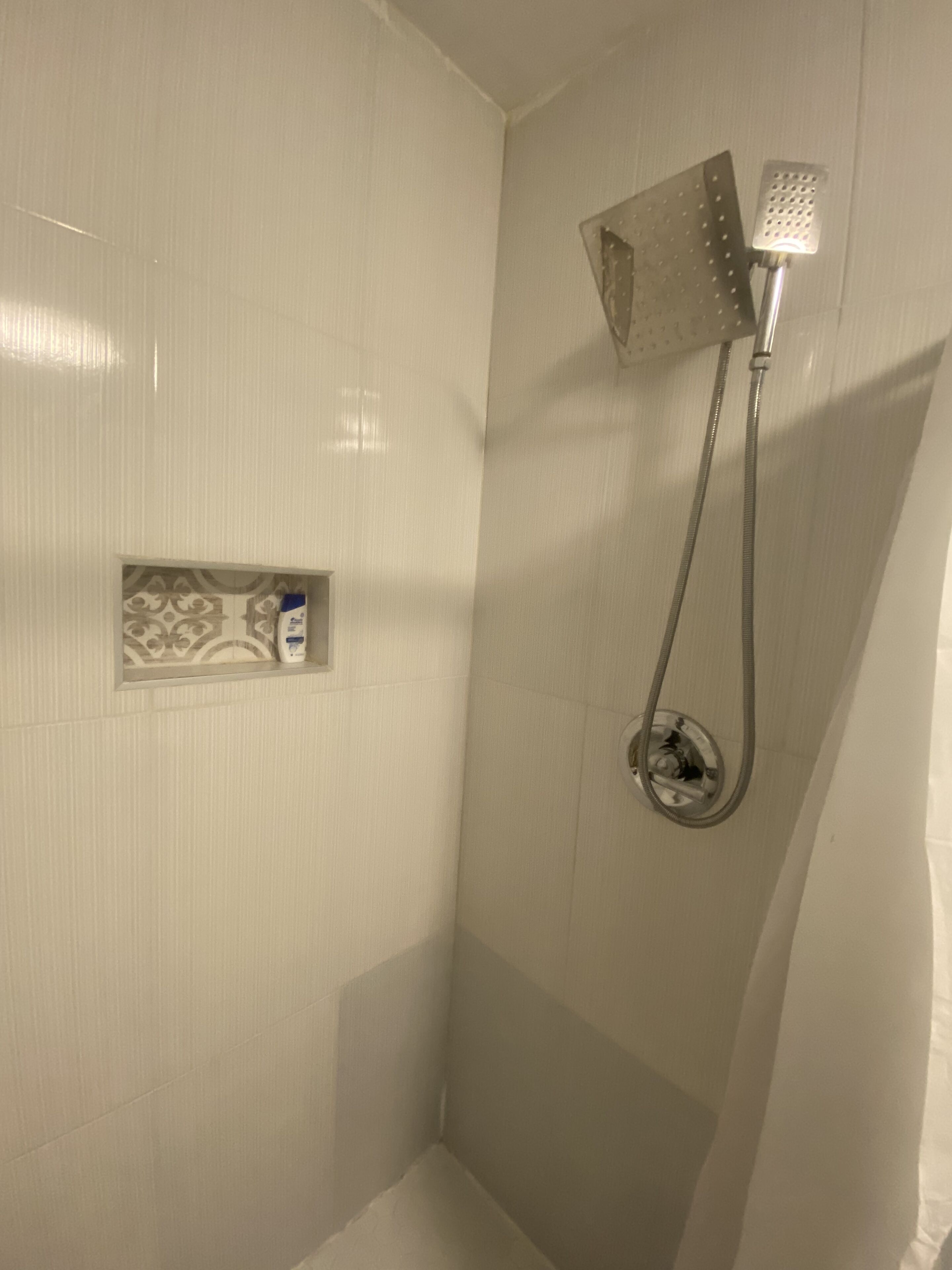 Ducha con cabezal de ducha de mano y panel de control en la pared.