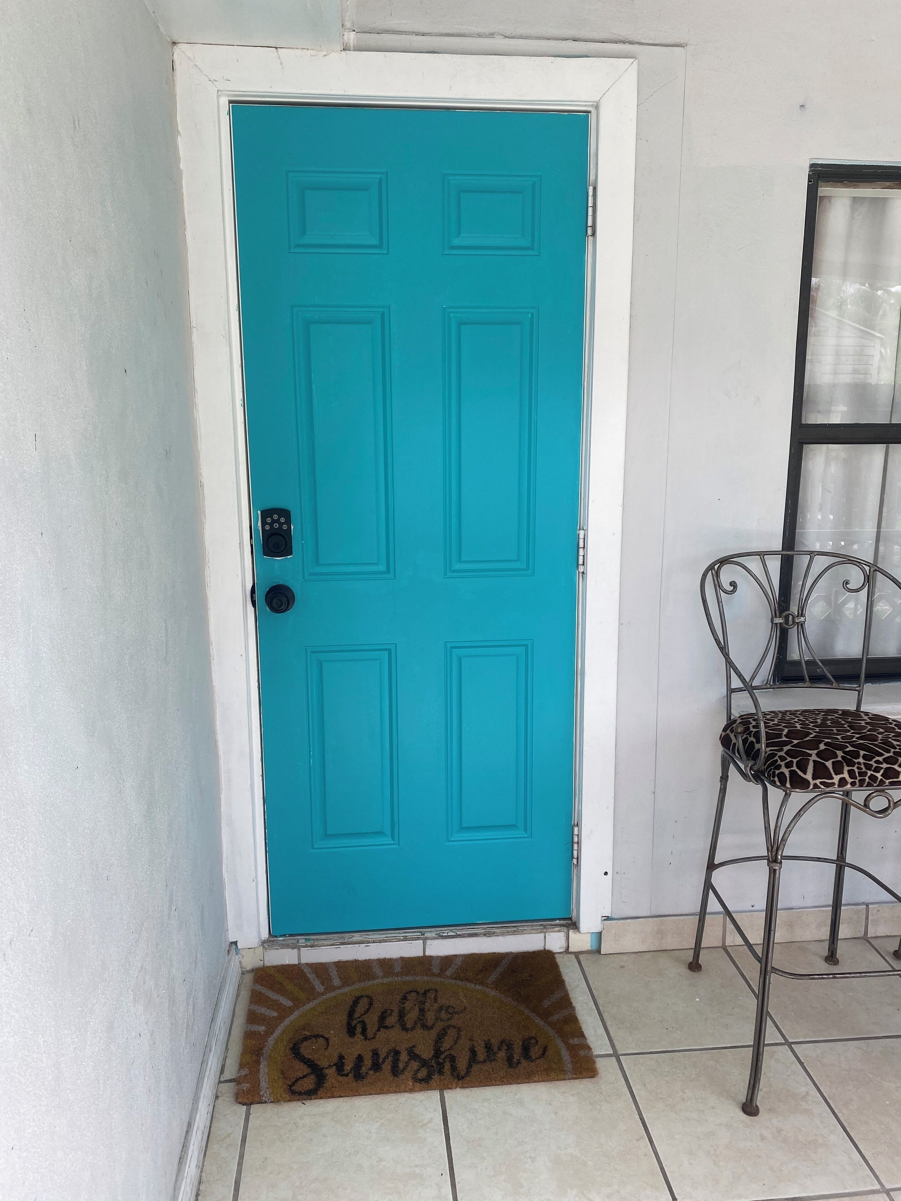 A turquoise door with a doormat that reads "hello Sunshine."