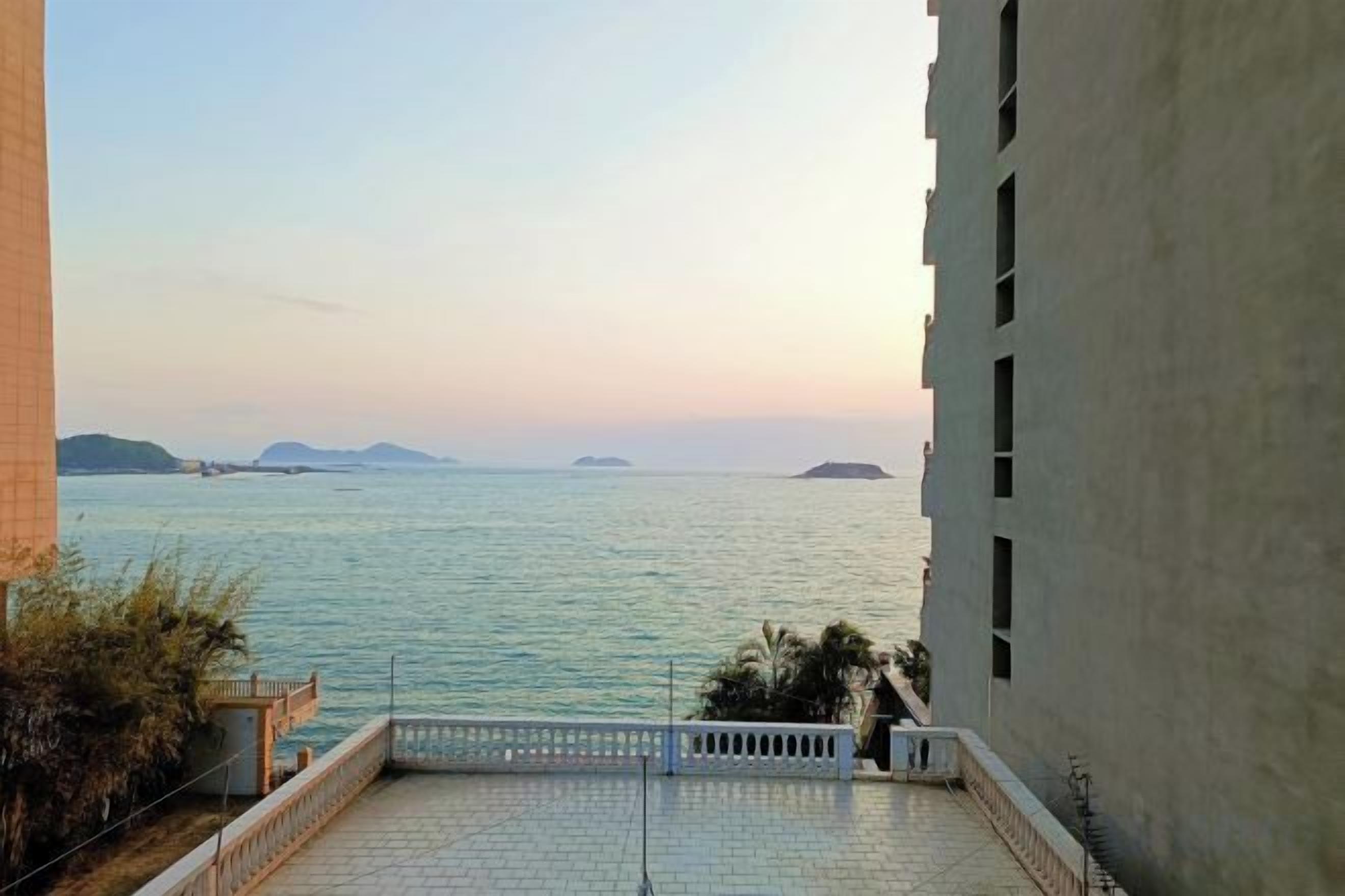Une vue depuis un balcon donnant sur une mer calme, avec des îles lointaines à l’horizon, un ciel dégagé et un bâtiment doté d’un balcon.