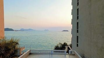 A view from a balcony overlooking a calm sea with distant islands, a clear sky, and a building with a balcony.