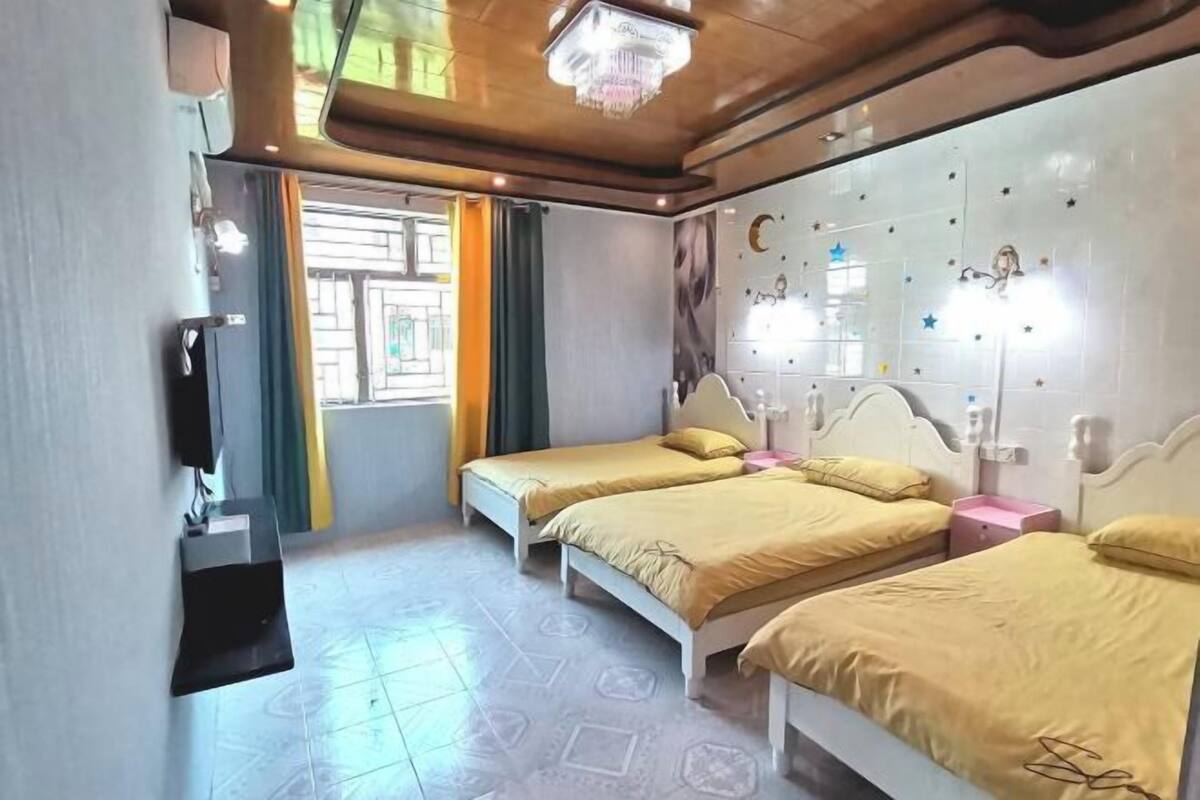 A hotel room with three beds, a TV, a chandelier, and a wall with decorative elements.