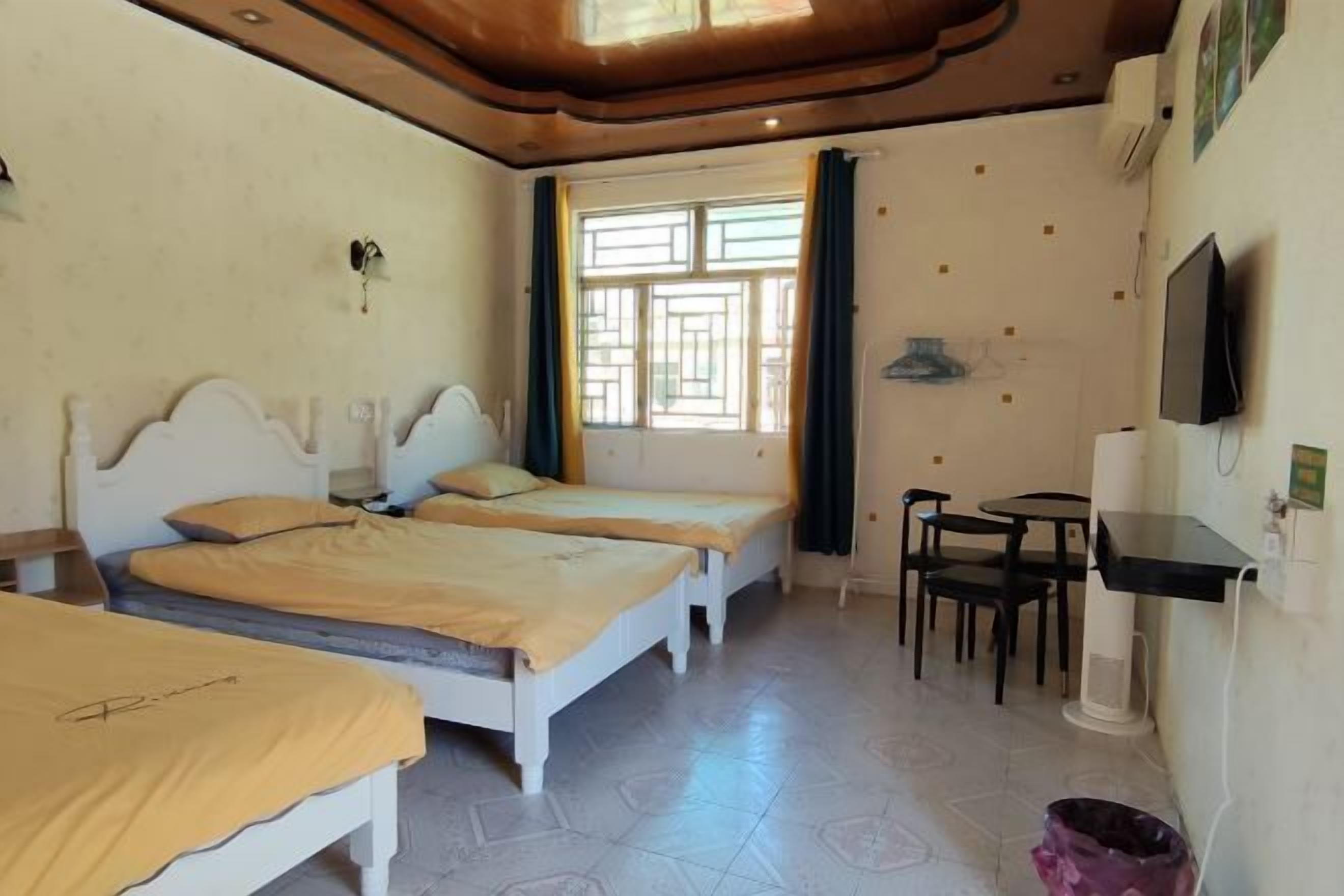 Une chambre avec deux lits simples, une petite table, un téléviseur et une fenêtre avec des rideaux.