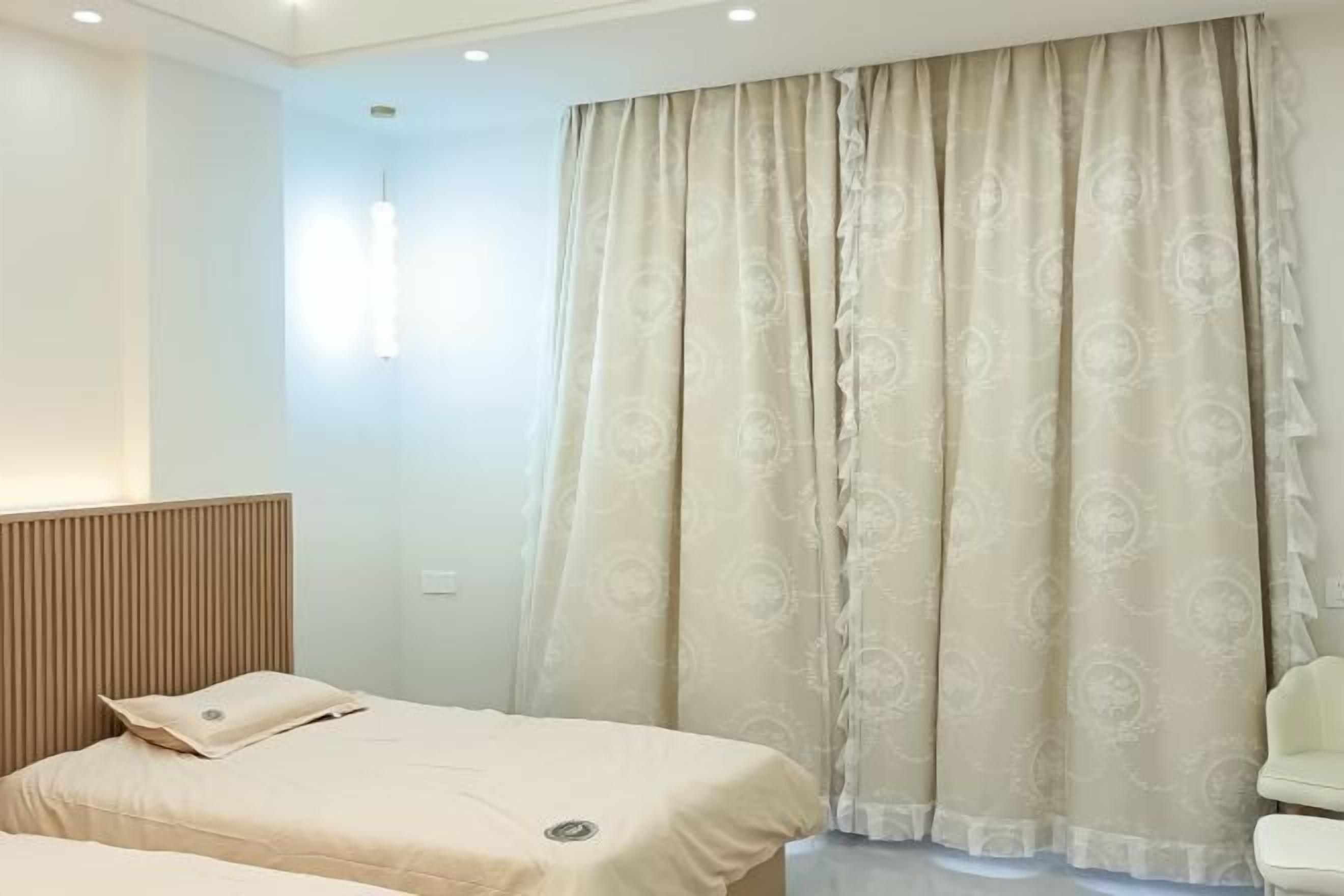 Een hotelkamer met een bed, nachtkastje, stoel en een raam met gordijnen.