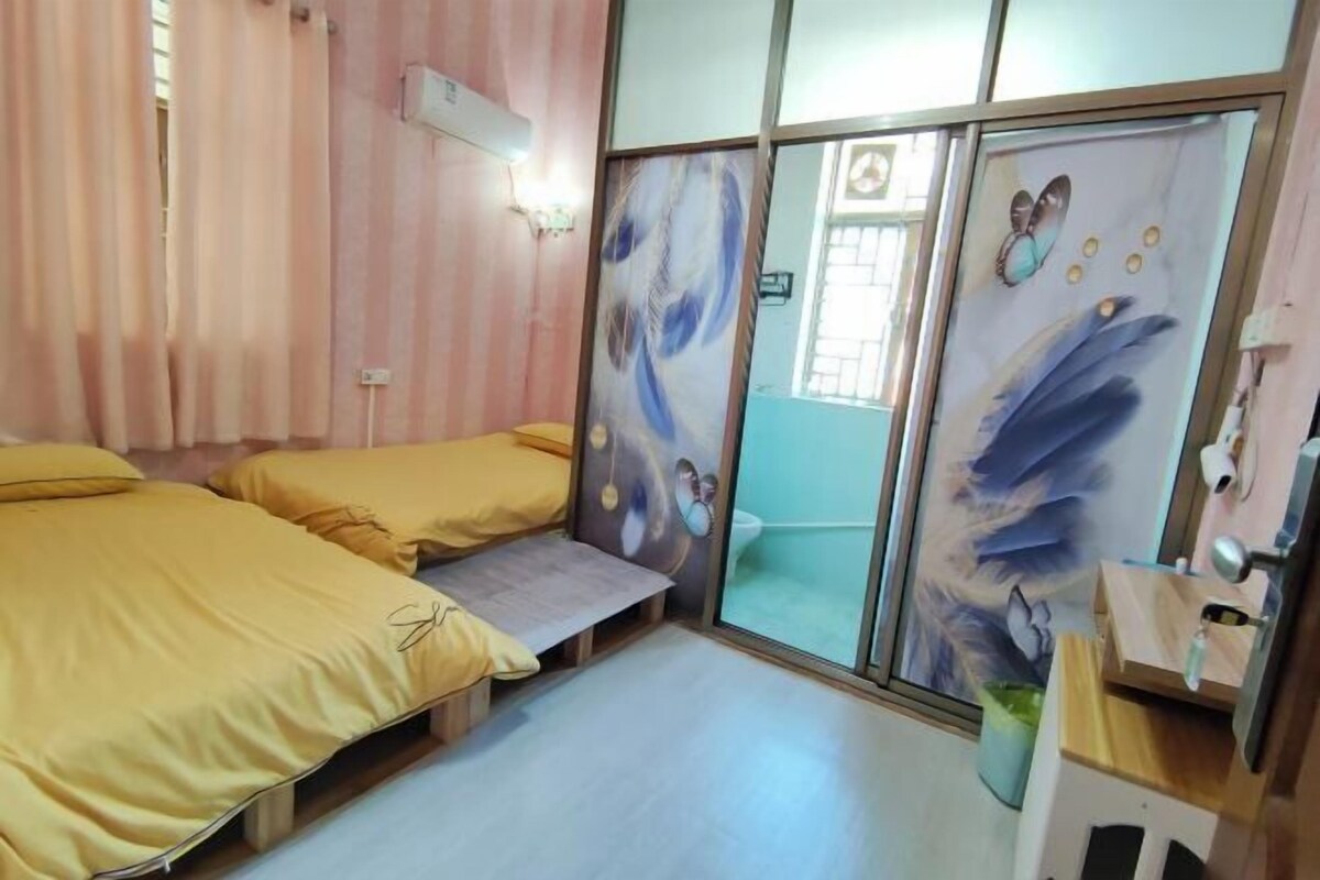 Ein Zimmer mit zwei Betten, einem kleinen Tisch, einer Schiebetür mit Kunstwerk und einem Vorhangfenster.