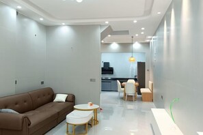 Ein modernes Wohnzimmer mit einer braunen Couch, einem kleinen runden Tisch und einer Küche im Hintergrund.