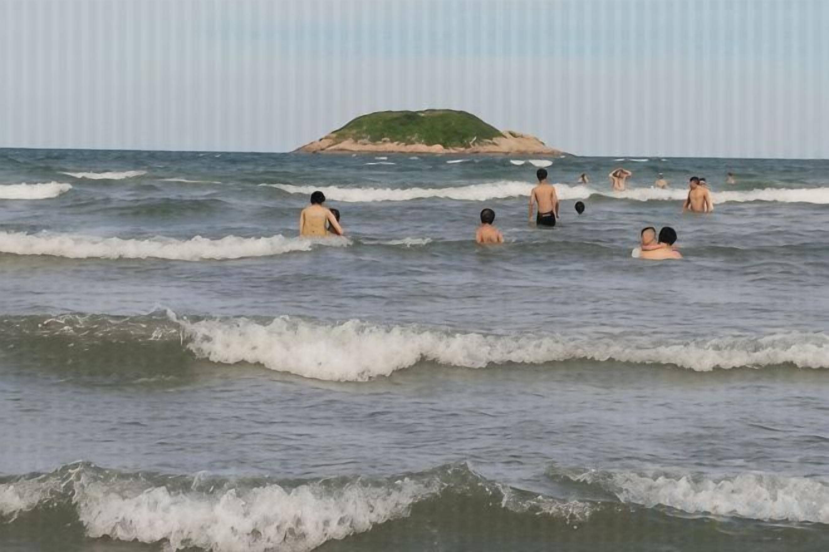 Ein Strand mit badenden Personen und einer kleinen Insel in der Ferne.