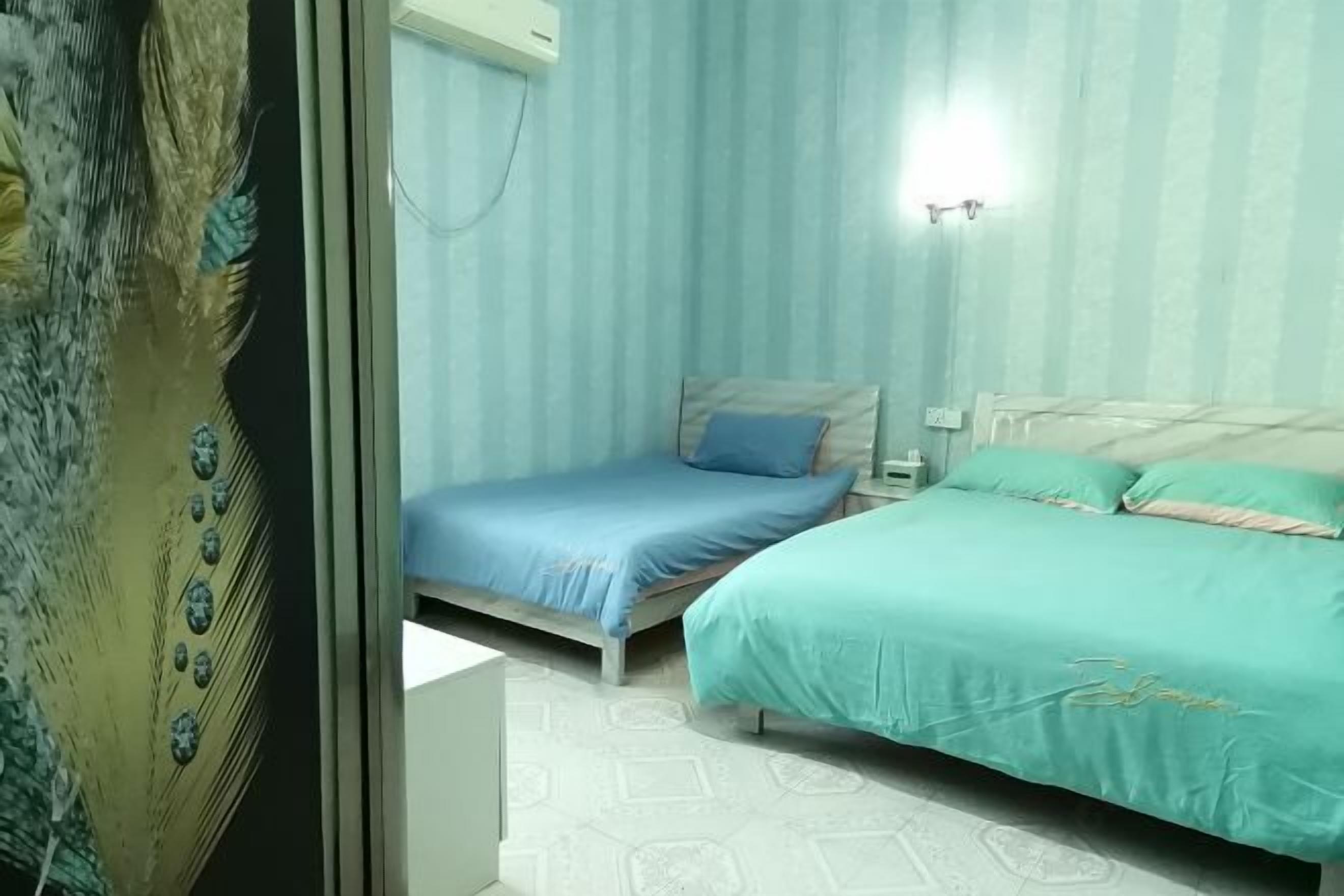 A bedroom with two beds, a peacock feather artwork on the left, and a light blue striped wall.