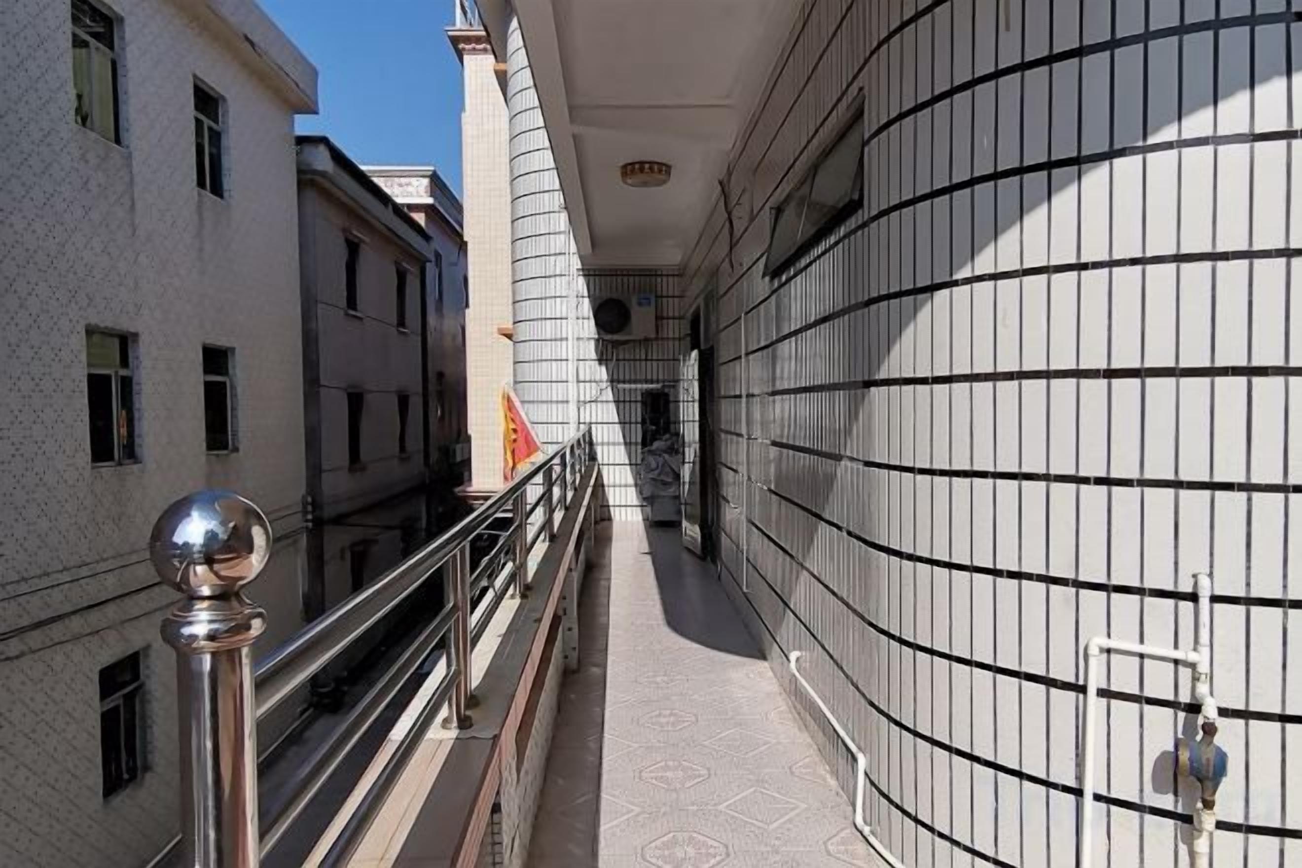 A corridor with a metal railing, a tiled floor, and a building facade with a grid pattern.