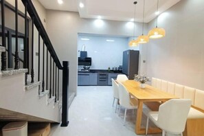 Ein moderner Essbereich mit Holztisch und weißen Stühlen, eine Treppe mit schwarzen Geländern und eine Küche im Hintergrund.