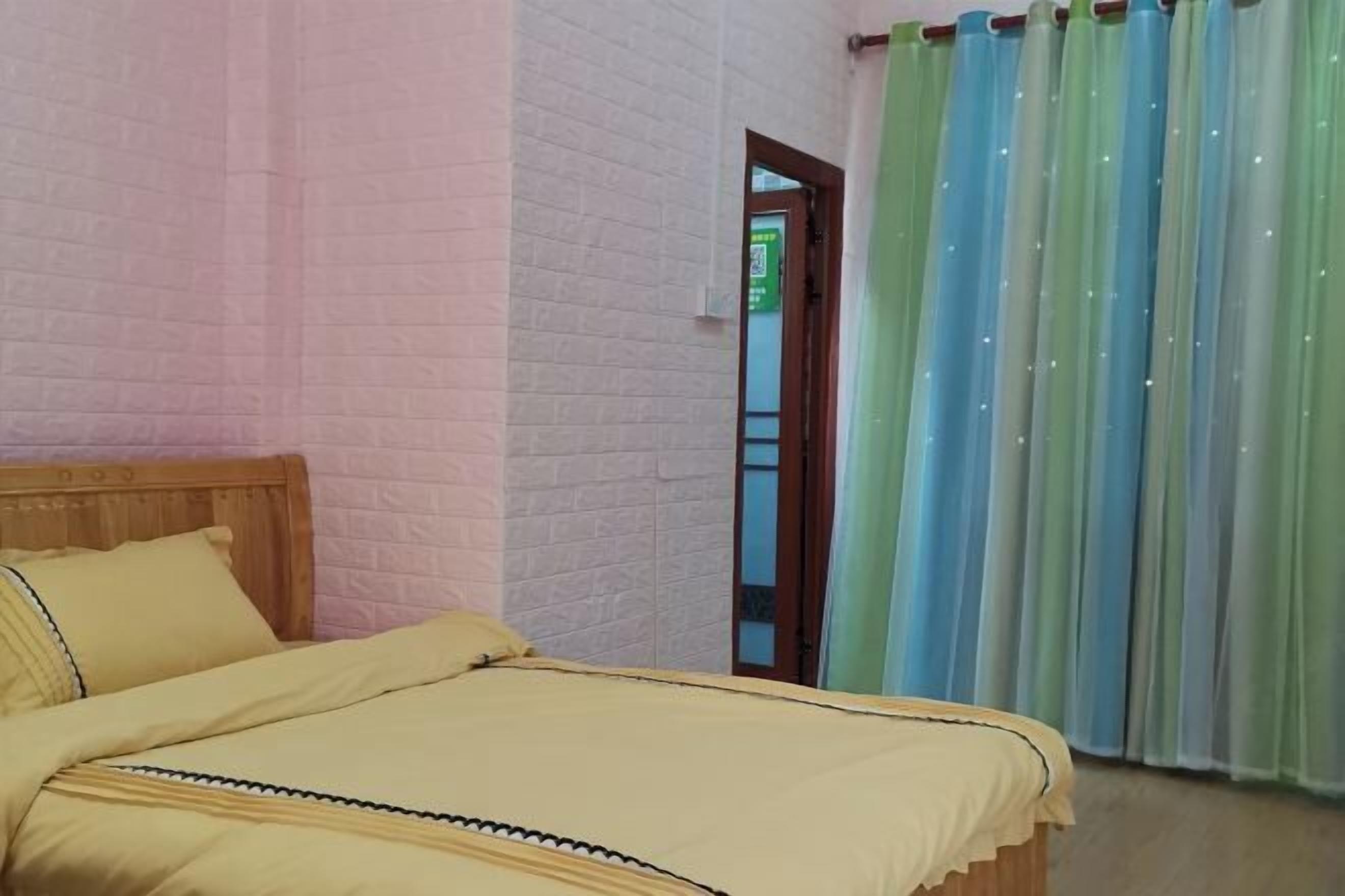 A bedroom with a wooden headboard, a bed with a yellow bedspread, and a window with green and blue curtains.