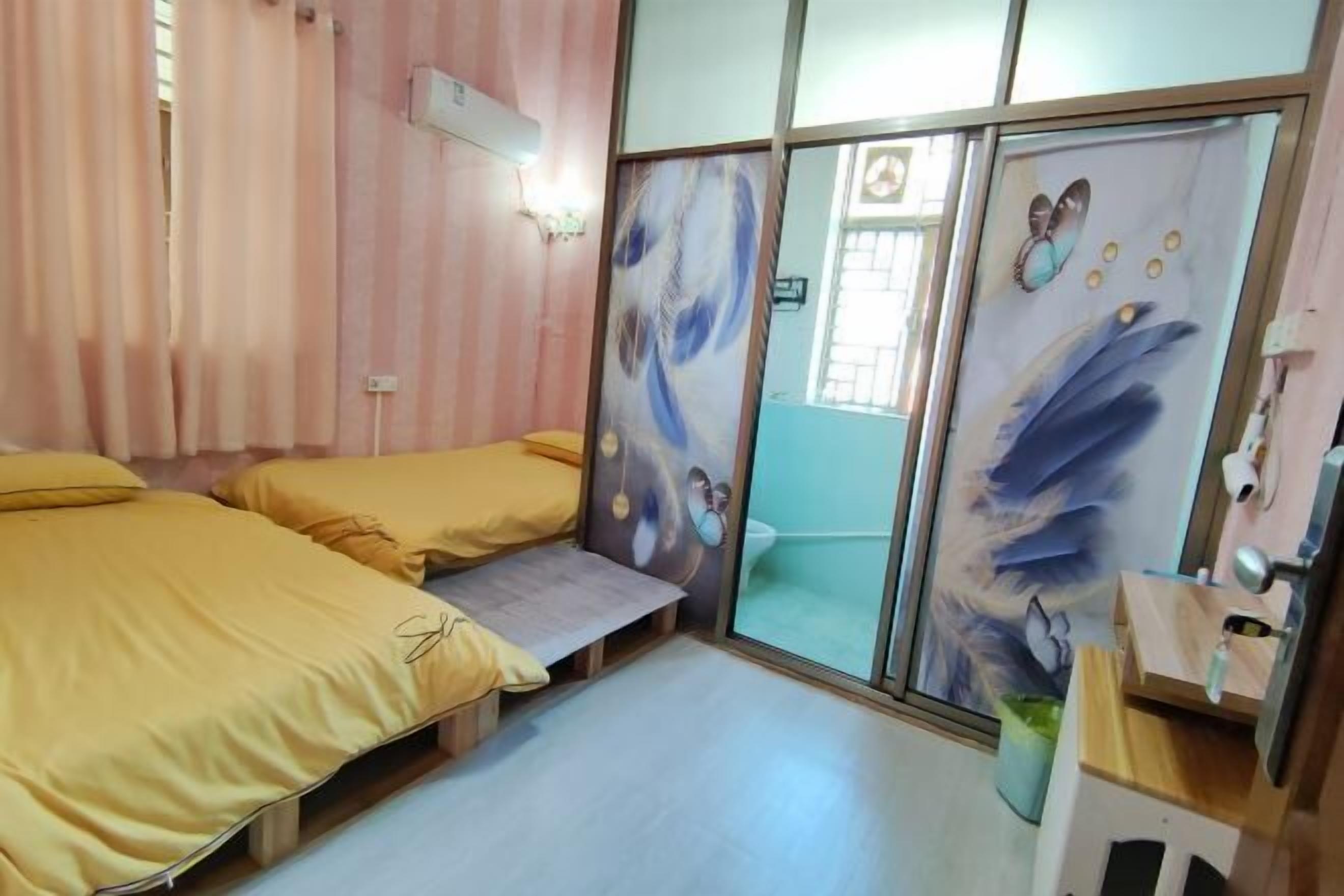 A room with two beds, a small table, a sliding door with artwork, and a window with blinds.