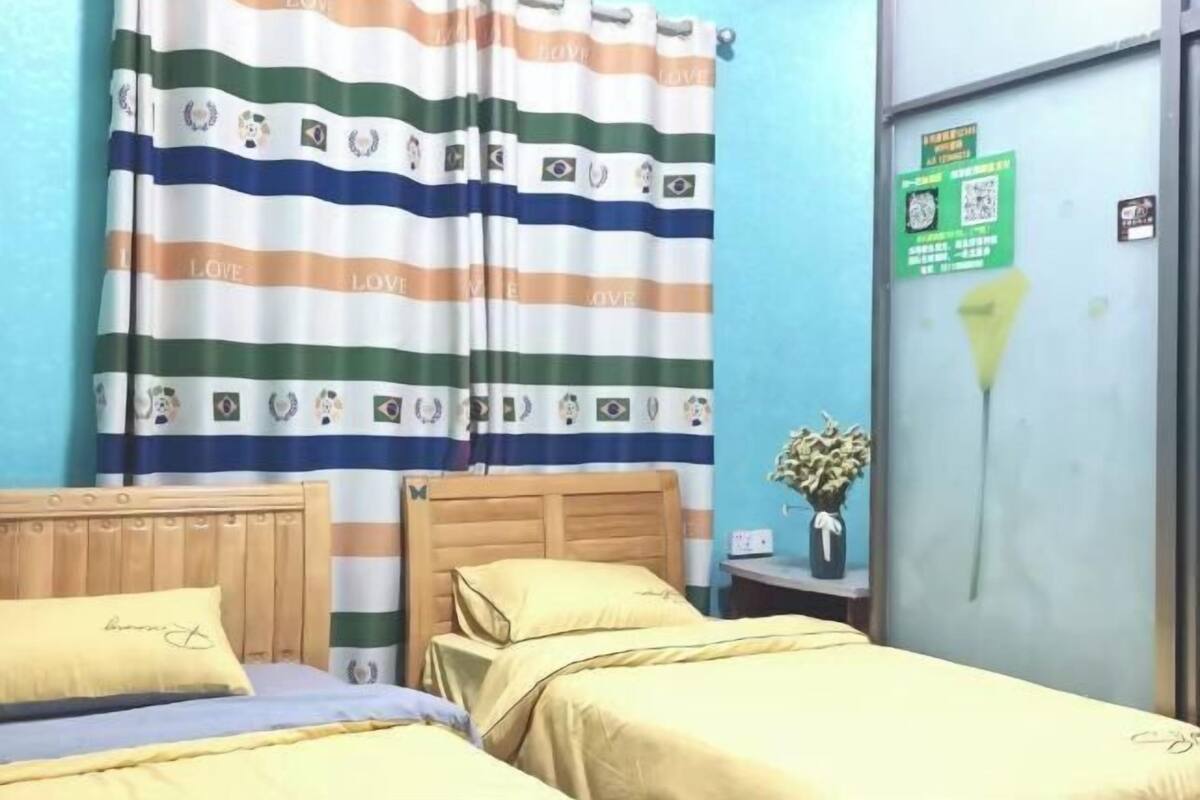 A hotel room with two beds, striped curtains, a wooden headboard, a bedside table with a vase of flowers, and a green sign on the door.
