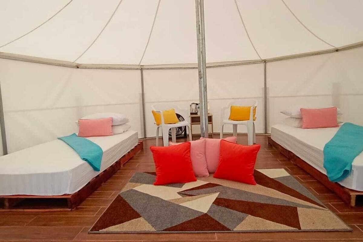 Eine Zelthütte mit zwei Betten, jeweils ausgestattet mit Kopfkissen und Decken. In der Mitte befindet sich ein kleiner Tisch und zwei Stühle.