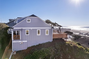 Overlooking the ocean, this house features a spacious balcony with a wooden railing and deck.