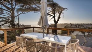 Um deck de madeira com mesa e cadeiras de vime, com vista para a água e edifícios.