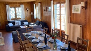 A wooden interior with a dining table set for four, a sofa, and a window with curtains.