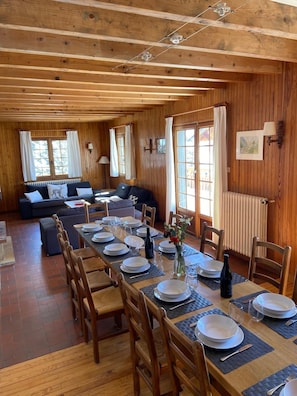 A wooden interior with a dining table set for four, a sofa, and a window with curtains.