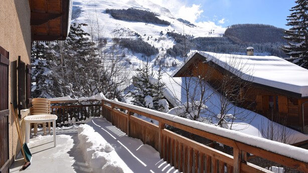 A wooden balcony with a view of a snow-covered mountain and forest.