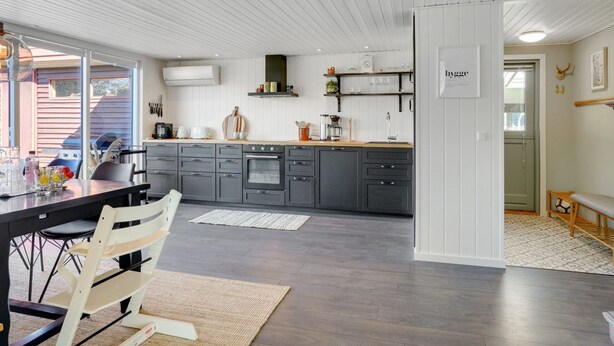 A modern kitchen with dark grey cabinets, a wooden countertop, and a built-in oven. There is a dining area with a table and chairs, and a large window providing natural light. - "Sveina" - 600m from the sea by Interhome (Hadsund)