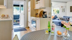 Eine kleine Küche mit Herd, Backofen und Kaffeemaschine, die in einen Essbereich mit gedecktem Tisch für zwei Personen übergeht.