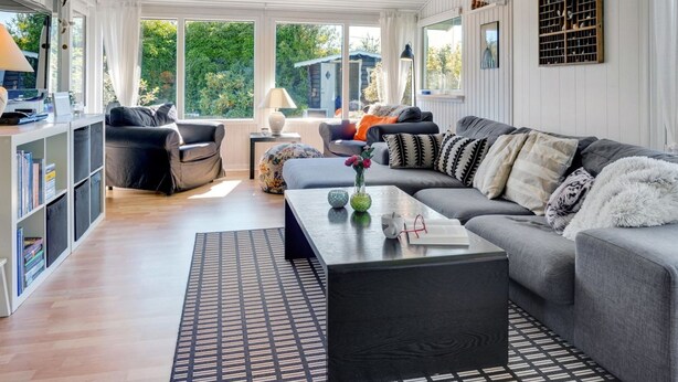 Ein modernes Wohnzimmer mit einem grauen Sofa, schwarz-weißen Kissen, einem Couchtisch mit Vase und Buch sowie einem Bücherregal.